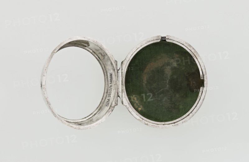Pocket watch by John Bushman 1692–1720. Silver pocket watch in three cases: outer case covered with leather, rim decorated with studded silver rosettes; middle and inner cases plain. Underside of inner case stamped with casemaker's initial H and number 3081. Transparent lid. Silver champlevé dial with Roman numeral hour markers and Arabic minute markers in oval reserves on a matte background; central circular reserve with the watchmaker's signature on two semicircular plates reading BUSHMAN and LONDON; date window at the bottom. Steel hands with openwork hour hand. Movement with plate skeleton, spring drive, worm gear, and Gall chain; spindle escapement. Gilded lower plate with an openwork English-style bun in the form of a wreath filled with acanthus tendrils and an openwork grid, connected by a mascaron mask with an openwork bun foot. Hair adjustment is a rotating silver-plated dial with a scale I–VI. Engraved on the plate in italics: Jn Bushman 3081 / LONDON. Circa 1700, London, Eng...