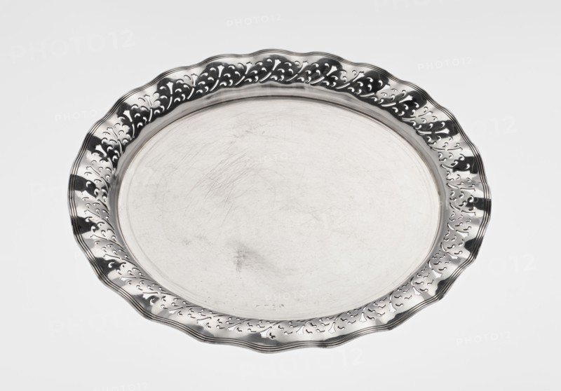 Circular tray, scrap, purchased ca. 1908, England, Birmingham; dish, diameter 32 cm, weight 722 g, A round metal tray with a scalloped rim and decorative cutout pattern around the edge, shown against a light background; the tray surface is smooth with visible scratches and wear, and the metal appears shiny with reflective areas in silver and darker gray tones.