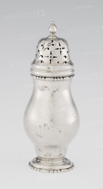 Powdered sugar bowl, powdered sugar bowl with domed openwork cover topped with a bowl; pear-shaped powdered sugar bowl on a circular profiled foot, with a domed openwork cover topped with a bowl. Openwork, sugar vessel, astargal ornament. Maker: Burbidge, Richard 1847–1917, goldsmith. Manufacturer/seller: Harrod's Stores Ltd London, fl. from 1849. Date: 1913/1914. Place: London, England. Form: dish. Dimensions: height 15 cm; diameter 5.9 cm; weight 152 g. Purchase provenance: scrap — purchase., A single metallic container with a rounded body and a removable perforated domed lid sits against a plain light background; the object is primarily silvery with areas of darker tarnish and small spots, the lid shows decorative cutout patterns and a small finial on top, the body tapers toward a stepped circular base that has a beaded edge, and the overall surface displays slight scratches and blemishes in shades of silver and gray.