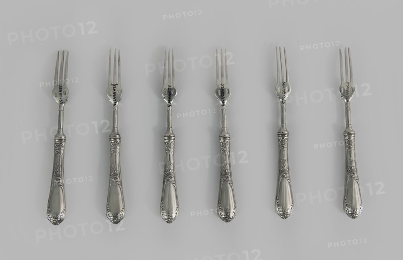 Six fruit forks by Adam Nagalski 1862–1944, 1915–1920, Poland, Warsaw; cutlery; height 16.5 cm, width 1.8 cm, A row of several ornate metal forks is laid out against a pale gray background, each fork showing a shiny silver finish with decorative engraved handles featuring floral and scroll motifs; the tines and necks of the forks are slender and polished, and the overall colors visible are shades of silver and gray.