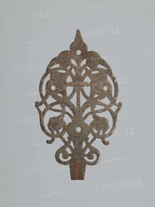 Hinge end for a chest;, Fittings, hinge end from a pair, in the form of an openwork rounded plaque with a tendril motif and two male masks among the twists. Hinge cut off; perhaps originally a disc hinge with a sleeve at the end of the plate or a strap hinge in the form of a clock hand. 17th century, Poland; Central Europe. Door fittings. Height 21.5 cm, width 12.5 cm, depth 0.2 cm., A flat, ornate object with a symmetrical, openwork design in a brownish metallic color set against a pale gray background, featuring a pointed top, curved scroll-like elements, stylized animal or bird head shapes integrated into the scrolls, circular cutouts, and signs of surface wear and lighter discoloration in places.
