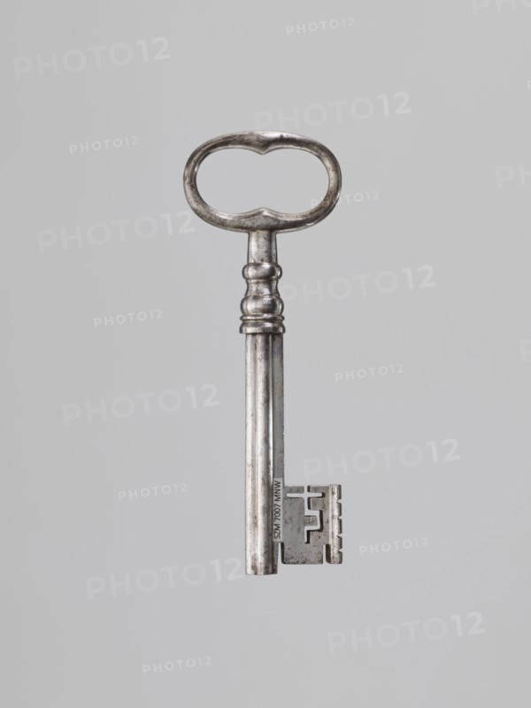Iron key, locksmithing. Key with a tubular club-shaped shaft, with a feather widened at the end. Shaft joint with profiles, oval handle with bulges on the shorter axis. 1st half of the 19th century., and place. Height 12.4 cm, width 4.5 cm, depth 1.2 cm., A single metal key is centered against a plain light gray background; the key has a rounded, oval-shaped bow with a slightly irregular inner edge, a short neck with a few raised rings, a long cylindrical shaft showing areas of darker and lighter silver tones, and a rectangular bit with notches and a stepped profile. The visible colors are silver and light gray.
