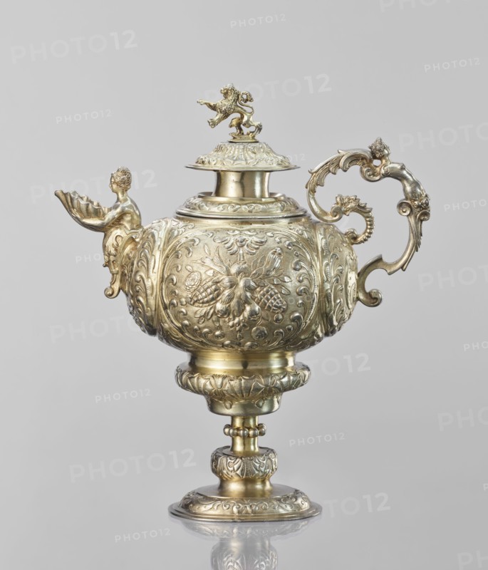 Water tincture, Schweiger, Matthias fl. ca. 1623–1635, goldsmith; herms decorative elements; lions; flowers ornament; fruit ornament; acanthus ornament. Jug with a spherical belly decorated with repoussé bouquets of flowers and fruit in acanthus reserves; on the side a spout in the shape of a female half-figure holding a conch; on the axis a plastic handle formed of channel sections connected by a winged herm of a woman. The cover is topped with a plastic lion standing on its hind legs. 1630–1635, Augsburg, Germany. Vessel; height 28 cm, width 14 cm, depth 30 cm., A single ornate vessel with a lid and pedestal is shown, rendered in a metallic gold color with areas of lighter and darker gold tones; the body is rounded and richly decorated with embossed floral and scroll motifs, and the surface has a reflective sheen. The lid is topped by a small sculpted figure of a lion in the same gold color, and the spout area features a sculpted figure of a partially visible human form holding a she...