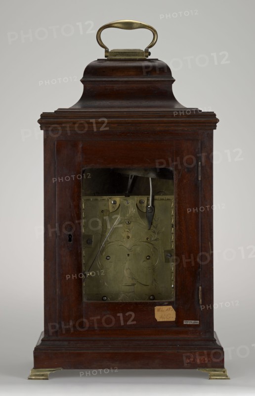 Grandfather clock, rocaille ornament, winged angel heads, bracket clock type, decorative birds; mahogany-veneered wooden cuboid glazed cabinet on a profiled plinth with four brass legs; rectangular raised profiled finial, concave lower sides, rounded upper section, brass knocker handle at top. Glazed rectangular front door topped by a semicircular arch with applied plaques at corners depicting winged angel heads and an acanthus twig; lockable door with preserved keyhole and brass escutcheon. Side walls closed with semicircular arch; rectangular hinged rear door. Movement: plate skeleton with verge spindle escapement, striking function and pendulum. Silvered brass dial with engraved hour ring Roman numerals and minute ring Arabic numerals; date aperture with Arabic numerals for day of month. Steel hands: minute hand with O-ring at base and straight tip, shorter openwork hour hand. Small engraved strike/silent disk with steel hand to enable/disable striking. Central keyholes in dial one ...