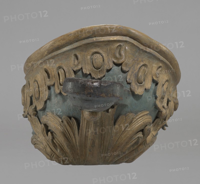 Sleigh, rococo two-seater, carved, polychrome, gilded; 3rd quarter of the 18th century, Poland . The sleigh is in the shape of a gondola made using the dugout canoe method, painted blue, with a wavy upper rim highlighted by a half-cylinder and channel sections with rocaille motifs. The front is a mascaron painted red, framed with acanthus leaves; at the rear is a trestle originally upholstered with a carved acanthus underneath. Inside the sled are four sockets for connection with skid supports. Materials/technique: carved, polychrome, gilded. Dimensions: height 57 cm, width 208 cm, depth 68 cm., A carved decorative object photographed against a plain gray background, showing the upper portion of a bowl-like form with ornamental leaf and scroll motifs. The object has a rounded rim and an outward-facing flared element, with layered carved foliage along the lower edge and repeated rounded scroll details along the upper band. Visible colors include muted gold on the carved details, a weath...