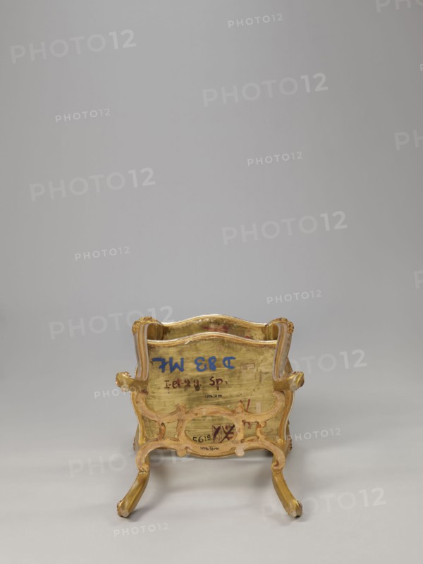 Side table, equipment of representative buildings of the Republic of Poland 1918–1939, unknown origin, plant decoration, acanthus ornament, volutes, neo-rococo style, 3rd quarter of the 19th century, Warsaw, furniture — table; height 77.3 cm, width 50 cm, depth 40 cm., A small ornate chair shown from the back with a carved frame and curved legs, featuring a worn gold finish with areas of exposed wood tones and touches of muted pink; the background is a smooth light gray and the floor is a slightly darker gray.
