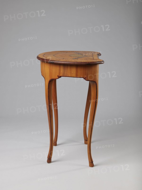 Table, Kidney-shaped auxiliary table supported by four slender, slightly curved S-shaped legs framed and bound with a rosewood ribbon; feet in the form of black-stained hooves. Front frame concave with a small central drawer. Tabletop decorated centrally with a fan enclosed by four fields separated by a ribbon of irregular, rounded outline and a narrow crosswise frame. Fan setting inlaid with mother-of-pearl rosettes and bound with tin veining; lower part of the fan features alternating light and dark areas. Tabletop edge veneered with yew solid wood. Mortise lock, single-bolt with brass plate. Circa 1730–1750, possibly Saxony. Furniture table. Dimensions: height 72.5 cm, width 71.5 cm, depth 46.2 cm., A small wooden table with a rounded top and slender, curved legs stands against a plain gray background; the table shows warm brown and honey-colored wood tones with darker brown edging and decorative inlaid patterns on the top, and the legs have subtle dark accents along their inner cur...