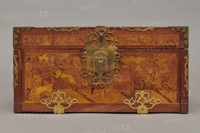 Casket, Repossession provenance. Sleigh, deer, hunters, hounds, riders. Baroque style. Cuboid case inlaid with figural scenes, with openwork brass fittings. Front wall of the body shows a deer hunt with dogs; on the lid, in an oval field, a sleigh drawn by a deer. Inside the body, under the chamber floor, are three drawers middle one smaller accessible after folding down the front wall. Lid contains a compartment closed with a plate on brass hinges. Fittings cut from thick brass sheet placed on the edges of the lid and the corners of the body. Bottom and back wall fastened with strap hinges with decorative openwork finials visible from the back of the lid and at the bottom of the front wall. Mortice-type lock with two catches mounted on the bottom of the lid. Dated 1720–1740, Germany. Furniture — storage furniture. Dimensions: height 21.6 cm; width 42.5 cm; depth 27.4 cm., A rectangular wooden chest with a warm brown and amber marbled surface, decorated with ornate brass fittings and e...