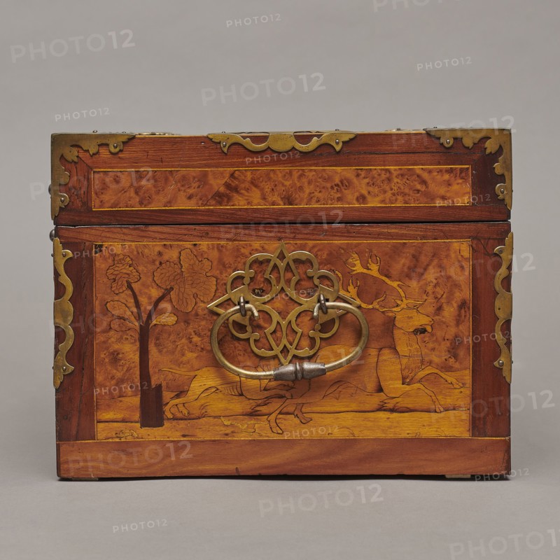 Casket, Repossession provenance. Sleigh, deer, hunters, hounds, riders. Baroque style. Cuboid case inlaid with figural scenes, with openwork brass fittings. Front wall of the body depicts a deer hunt with dogs; lid shows, in an oval field, a sleigh drawn by a deer. Inside the body, under the chamber bottom, are three drawers middle one smaller accessible after folding down the front wall. Lid contains a compartment closed with a plate on brass hinges. Fittings cut from thick brass sheet placed on the lid edges and body corners. Bottom and back wall fastened with strap hinges with decorative openwork finials visible from the back of the lid and at the bottom of the front wall. Mortice-type lock with two catches mounted on the bottom of the lid. Date: 1720–1740. Place of origin: Germany. Furniture — storage furniture. Dimensions: height 21.6 cm; width 42.5 cm; depth 27.4 cm., A small rectangular wooden box sits on a neutral gray surface against a gray background, showing a front face wit...