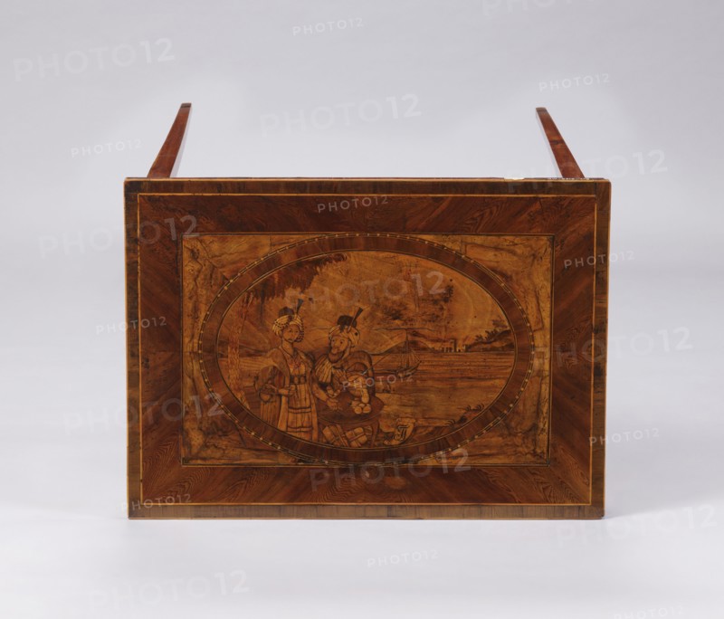 Table, figures in Eastern costume, figures against a landscape, palm trees, seascapes, sailing ships, monograms. A Classicist rectangular inlaid table, supported by four slender, angular, converging legs. On the tabletop a rectangular field framed by a wide border with light veining, containing an inscribed oval bordered by a wide ribbon and veining. Inside the oval is a seaside landscape with a palm tree on the left, a castle on the right, and two men in Eastern costume standing at a round table with dishes and fruit. Between the S-shaped legs are two bundles. At the bottom of the composition is a cartouche with the initials JJ or TT. Late 18th century, Poland, furniture, table. Dimensions: height 73.5 cm, width 63.7 cm, depth 46.3 cm., A rectangular wooden panel with a warm brown finish features an oval central inlay depicting two figures standing near a shoreline with a small boat and distant buildings; the panel shows grain patterns and darker brown border inlays, and the overall s...