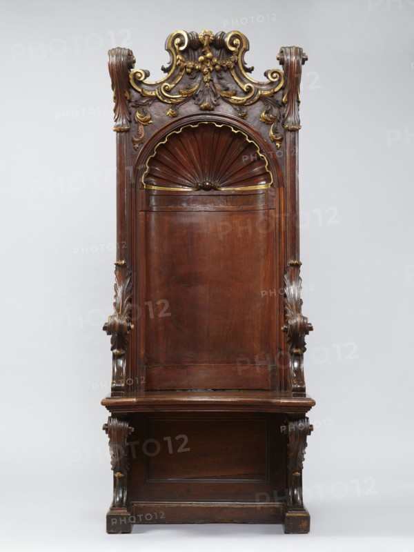 Church throne armchair, carved, mid-18th century, Italy. Seating piece furniture with two console supports for the board seat and a high rectangular backrest in the form of an aedicula topped with a volute top. Supported on a platform cut out in the shape of the letter U. Supports, sides, and lower part of the back have a frame structure. Seat has a concave outline with a profiled rim, lifting in the middle on hinges. The aedicula in the backrest is two-part, with a shell at the top framed by a profiled cornice. Lower side walls arch into the armrests. Upper seat supports, armrests, and side pinnacles are carved with volutes formed of acanthus leaves. Aedicula shell rim and volutes in the finial are gilded. Ornament: shells, acanthus, volutes; style: Baroque. Height 201.5 cm, width 81 cm, depth 59 cm., A tall carved wooden chair with a high back featuring an arched shell motif near the top and ornate scrollwork and foliage carvings along the crest and sides, with visible gilded highlig...
