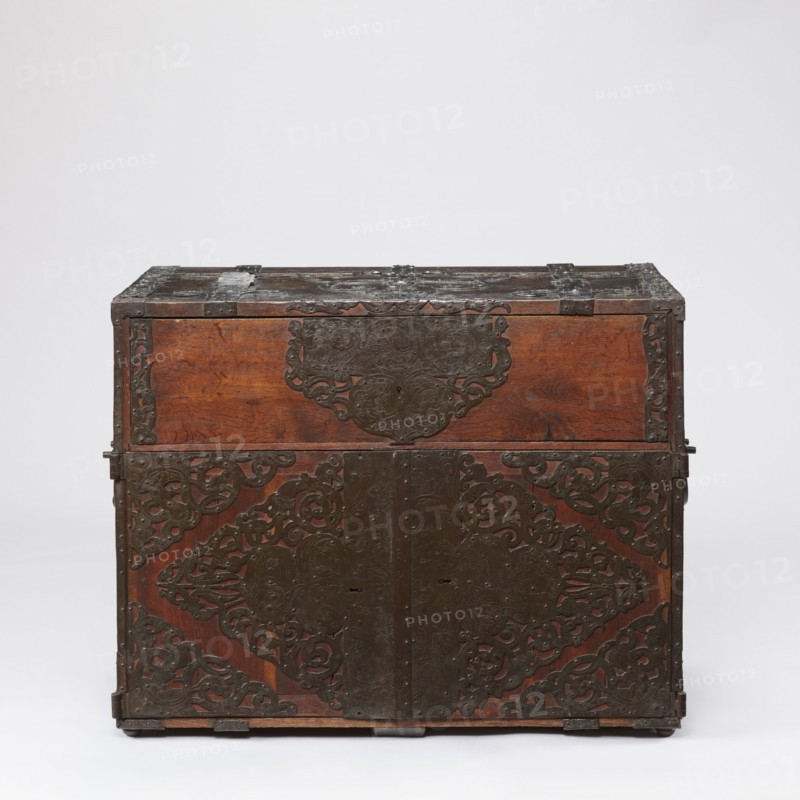 Cabinet, late 17th century, Northern Germany or Poland — cuboid storage piece height 70.1 cm, width 89.2 cm, depth 55.9 cm. Cabinet with a top drawer and double doors below, richly decorated with openwork engraved fittings bearing grotesque motifs, fantastic animals, grotesques, fantastic figures, plant tendril ornament, wickerwork ornament, and male figures. Door leaves veneered inside with rosewood and ebony in geometric arrangements divided by inlaid bone veins, with figures in engraved bone signed Hippocrates on the left and Hermes on the right. Behind the doors are twelve compartments. Drawer and door locks fitted with engraved steel plates; the drawer lock blocks the left door leaf. Steel hinges., A wooden chest with a rectangular shape and a hinged top sits against a plain neutral background. The wood shows a warm brown color with visible grain, and dark metal fittings and decorative plates cover much of the front and top. The metalwork is dark brown to black and features ornate...