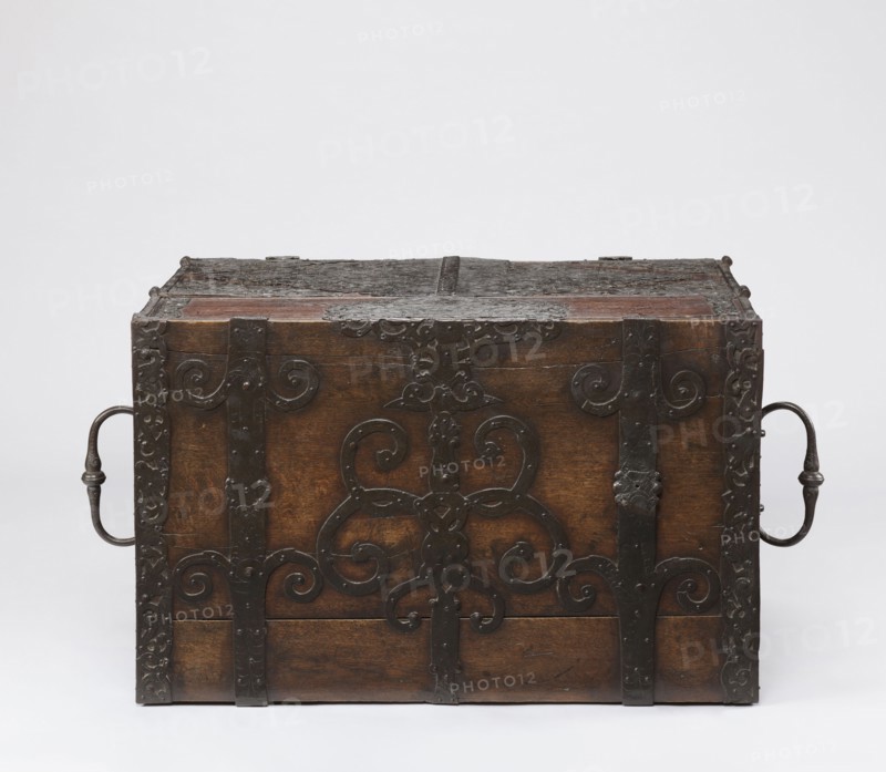 Cabinet, late 17th century, Northern Germany, or Poland, cuboid storage piece height 70.1 cm, width 89.2 cm, depth 55.9 cm. Cabinet with a drawer at the top and double doors below, richly decorated with openwork engraved fittings with grotesque motifs, wickerwork ornament, fantastic animals and figures, plant tendrils, and male figures. The inner door leaves are veneered with rosewood and ebony in geometric arrangements, divided by inlaid bone veins, with figures in engraved bone signed Hippocrates on the left and Hermes on the right. Behind the doors are twelve compartments. Drawer and door locks have engraved steel plates; the drawer lock blocks the left door leaf. Steel hinges., A wooden chest with dark brown tones and a weathered surface is shown, featuring ornate black metal straps and decorative scrollwork across its front and top, and a curved metal handle on each side that are dark gray to black in color; the background is a plain light gray to white.