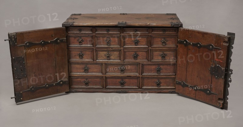 Cabinet, Baroque, 2nd quarter of the 17th century, Gdansk. A cuboid cabinet with a boarded body fitted with steel decorative strips, closed with double doors. Framed doors with single panels in the form of convex coffers glued at the mitre from richly profiled strips. Steel closing strip with a wavy outline, rectangular and trefoil-shaped angular fittings on the edges of the body, punched, fastened with headers. Inside: sixteen drawers arranged in five rows two in the top row, four in the two middle rows, three in the bottom rows. Drawer faces framed with profiled strips; three drawers in the middle row have numerous internal divisions. Walls connected with exposed diagonal dovetails; back joined to top and sides with dowels. Drawers with exposed diagonal dovetail joints; bottoms nailed. Side handles oval; drawer handles round with rosette-shaped plates. Hinges steel, strap-type with wavy outline. Both door leaves have steel mortise-and-apply locks with an additional hasp and covered k...