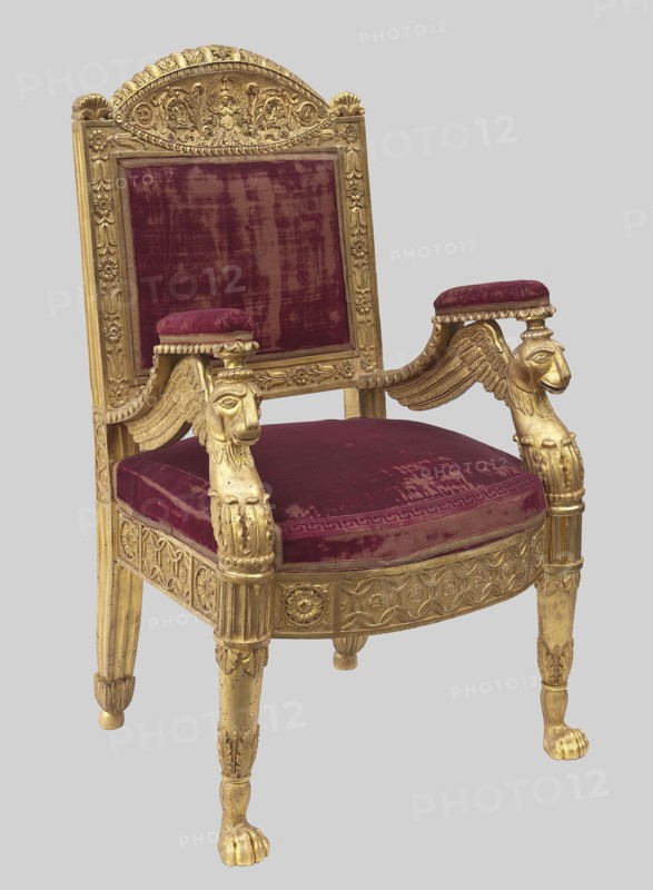 Armchair, ; griffins; Empire style; grotesques ornament; plant decoration; wickerwork ornament; kimation ornament. Straight backrest with a clearance, slightly tilted, topped with a semicircular board. Padded armrests supported by griffins. Trapezoidal seat with high frames front arched. Straight, turned front legs ending in lion paws. Early 19th century, Europe. Piece of furniture, seating piece. Height 108 cm, width 69 cm, depth 54 cm., An ornate armchair with a carved wooden frame finished in gold and upholstered in deep burgundy velvet, showing a rectangular backrest with a decorative crest, padded armrests topped with burgundy cushions, arm supports carved as winged mythic heads, a padded seat cushion, carved apron and fluted legs terminating in paw feet; visible colors include gold and burgundy against a pale gray background.