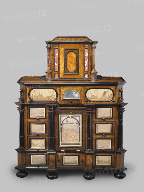 Cabinet, baroque style, columns, birds, early 18th century, Southern Germany, possibly Augsburg, piece of furniture, storage piece, height 114 cm, width 92 cm, depth 41 cm, A wooden cabinet with a layered, symmetrical design in warm brown and darker brown tones, accented with black trim and glossy black rounded feet; the upper section has a central rectangular raised compartment flanked by short columns with reddish-brown inlaid panels and lighter wood veneers, and the lower wider section features a central door with an arched framed panel showing a worn lighter wood scene, surrounded by paired dark columns and multiple small framed drawers on either side with lighter inset panels, plus a row of oval framed panels along the top front, all showing signs of age and wear and set against a pale grey background.