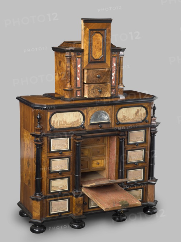 Cabinet, baroque, columns, birds, early 18th century, Southern Germany, Augsburg, piece of furniture, storage piece, height 114 cm, width 92 cm, depth 41 cm, A wooden cabinet with a warm brown finish and darker brown and black trim, featuring a stepped upper section with a central vertical panel and a pair of small drawers, flanked by narrow columns and panels with reddish accents; the midsection has a flat top surface and a row of decorative oval and arched panels above a recessed central compartment, which contains small wooden drawers and a pull-down shelf covered in worn red material with a brass latch, partially open; the lower section includes multiple small square drawers framed with dark trim on either side of the central opening, supported by turned black columns and resting on round black bun feet, with visible wood grain and areas of lighter tan and beige on several inset panels.