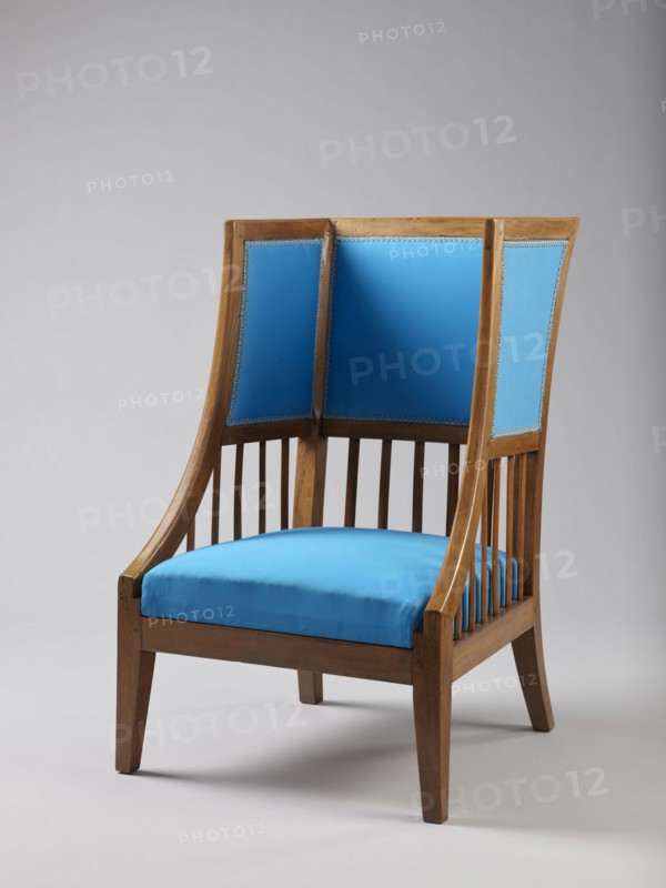Armchair Berzera, armchair with a slender backrest and sides equal in height, arching upwards and forming ears, with angular frame elements. Front legs converge, rear legs arch outwards. Narrow, straight frame; trapezoidal seat in the form of a removable cushion on springs. The upper part of the sides and the backrest, which is slightly wider in the upper part, are upholstered; the lower part is filled with vertical slats. Frame elements are additionally connected with single pegs. ca. 1820; possible origin: Warsaw, Vienna, or Lesser Poland. Piece of furniture seating piece. Dimensions: height 86.5 cm, width 54.8 cm, depth 61.8 cm., A wooden armchair with a medium-brown finish and a high back featuring three vertical upholstered panels, upholstered in bright blue fabric with decorative trim, and a bright blue seat cushion; the chair has slender vertical wooden slats on the sides and slightly tapered wooden legs, set against a pale gray background with soft shadows on the floor.