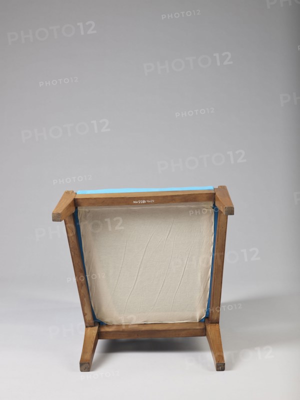Armchair Berzera, armchair with a slender backrest and sides equal in height, arching upwards and forming ears, with angular frame elements. Front legs converge, rear legs arch outwards. Narrow, straight frame; trapezoidal seat in the form of a removable cushion on springs. The upper part of the sides and the backrest, which is slightly wider in the upper part, are upholstered; the lower part is filled with vertical slats. The frame elements are additionally connected with single pegs. Ca. 1820; possible origins: Warsaw, Vienna, Lesser Poland. Piece of furniture seating piece. Height 86.5 cm; width 54.8 cm; depth 61.8 cm., A wooden framed stool or small chair viewed from the back, showing a rectangular canvas or fabric panel stretched within the frame; the wood is light brown with visible grain and some darker worn spots, the fabric is off-white or beige with subtle creases, and there is a strip of bright blue trim or tape along the top edge and inner sides; the background is a smooth ...