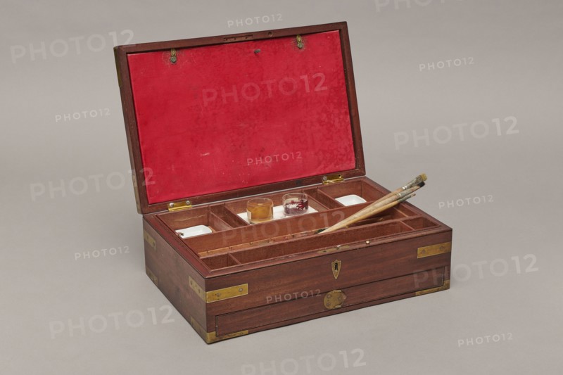 Painter's cassette, Travel painter's cassette, cuboid mahogany box with corners of body and lid reinforced with recessed brass sheets. Bottom of body has a drawer blocked by a brass pin inserted from above. Interior front has a row of compartments wider in middle, square at sides; behind them two removable containers—upper with five compartments three wide, separated by narrow ones, lower flat container with round sockets for faience paint vessels. Includes a steel pen holder; nine paintbrushes three flat, six round, various numberings; makers include Pelikan and Z. Dudek Warszawa; five cylindrical glass containers; eight porcelain bowls signed Cmielów / MADE / IN POLAND; a set of watercolors 54 pans; a stick of black Chinese ink; and a resin stick. Bottom backed with green cloth. Inside lid a cardboard and red leather file folder closed with two small brass bolts. Mortise lock with two sliding hook bolts; brass lock plate in form of an elongated disc. Brass and slate hinges. Brass dra...