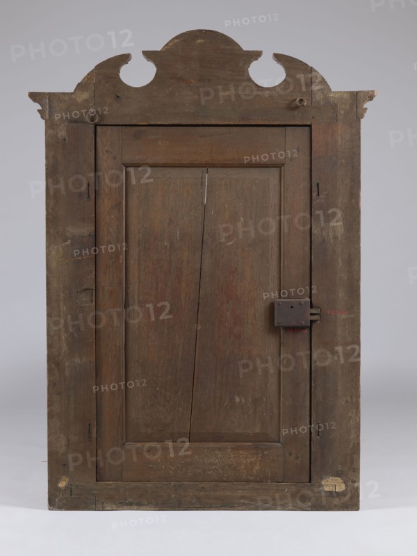 Built-in wardrobe front, gift, baroque, rococo, flowers, ribbon-pincer ornament, vases with flowers, pre-war, ca. 1762, Torun, fragment of furniture, height 138.5 cm, width 101 cm, depth 5.8 cm, A tall wooden door with a decorative curved pediment at the top, showing worn and weathered brown wood tones throughout; the door has a recessed central panel with visible wood grain and a vertical split, a simple frame with darker brown stiles and rails, and an old rectangular metal latch on the right side; the surface displays scratches, scuffs, and patches of lighter and darker brown, with a few small areas of beige and pale worn spots near the bottom and top edges, all set against a neutral gray background.