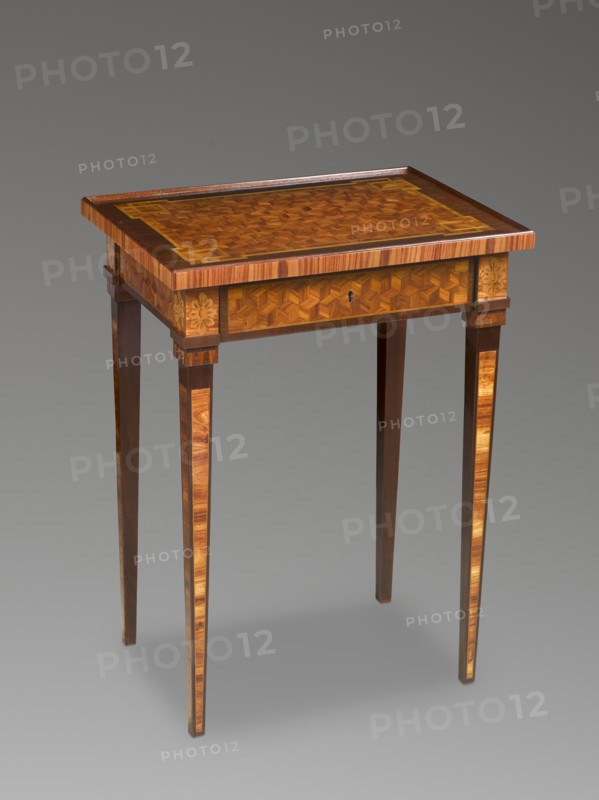 Table, classicism style, geometric ornament, rosettes ornament. Rectangular classicist table, inlaid, supported by four straight, converging legs. Leg surfaces decorated with rose-filled fields, edged with light veining. Leg cubes with inlaid rosettes. Straight frame repeating the outline of the top, with a drawer on the longer side, inlaid with the top into a cube in perspective. The top is bordered with a straight edge creating a kind of gallery. Semi-mortise, flush, single-bolt lock. Late 18th century, Central Europe. Furniture, table; height 71 cm, width 39.5 cm, depth 52.5 cm., A wooden table with a rectangular top featuring intricate geometric marquetry in warm brown and golden tones, a darker brown border along the top edge, slender tapered legs with vertical lighter wood inlays, a shallow apron with matching geometric inlay and small carved floral motifs at the corners, and an overall finish showing polished wood grain in shades of brown, amber, and tan against a neutral gray b...