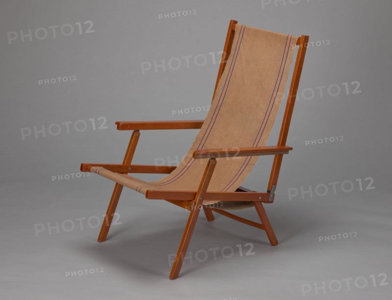 Deckchair, Polish Timber Industry, Czerski and Jakimowicz Lviv; furniture factory; 1929–1939,  furniture factory; lounge furniture, beach furniture, garden furniture, folding. Deckchair constructed from two different sized rectangular frames: the backrest smaller and the seat larger, connected by hinges, with canvas stretched over them. Frame elements except the turned rear leg connector and the doubled front seat stile are angular. The seat frame is supported on its shorter sides by two folding legs connected by a connector, the front extended into armrest supports. Armrests have hinges adjustable in three positions. Salmon-colored canvas fabric with vertical orange stripes framed by narrow blue stripes; attached to the underside of the upper backrest frame and the rear seat frame, sandwiched between the two front seat frames. Originally equipped with a separate footrest. 1938–1939, Lviv; seating furniture, piece of furniture. Height 84.2 cm, width 58.5 cm, depth 115.5 cm., A wooden f...