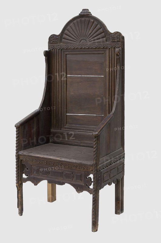 Armchair, geometric ornaments, plant decoration. Armchair with a high rectangular backrest, equally narrow seat and full sides, supported by four angular legs, richly decorated with bas-relief geometric and stylized plant motifs. Framed back, framed on the sides by fluted pilasters, profiled at the bottom, topped with a semicircular top. The top is decorated in the center with a fan with convex wings framed on the sides by wavy corners. The seat and sides are boarded. The sides are arched, with boarded armrests rounded at the corners. Below the frame are decorative strips with geometric fields, wavy at the bottom; the front is suspended, openwork on the sides, and the sides are applied. A strip with a cord motif is applied to the front edge of the legs and sides. Ca. 1635, Netherlands, England, Western Europe. Furniture — seating piece. Height 160.5 cm; width 70.3 cm; depth 51.5 cm., A tall wooden chair with a high back and armrests, carved with decorative patterns including a semi-cir...