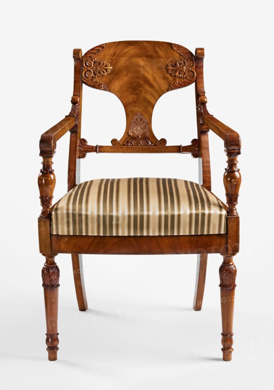 Armchair, Biedermeier style, acanthus ornament, message Office of the Council of Ministers, palmettes ornament. Front legs straight, turned in the form of a baluster; rear legs sabre-shaped. Trapezoidal seat, slightly bulging at the front. Wide side frames framing the seat cushion. Cushion rests on a pine frame, upholstered in green-striped fabric. Backrest composed of angular, S-shaped side stiles, a lower crossbar, and a rounded central board placed between them, narrowed at the bottom, straight in line with the back. Backrest stiles widened in the lower section, ending at the top with a forward-curved volute. Armrests angular, ending in a volute at the front, and with a rolled acanthus leaf at the backrest. Armrest supports turned in the form of a baluster. Polished frame enriched with woodcarving — acanthus leaves on the upper part of the front legs, antemion and symmetrical S-shaped beams at the bottom of the backrest board, scrollwork at the ends of the backrest crossbars. 1830–1...
