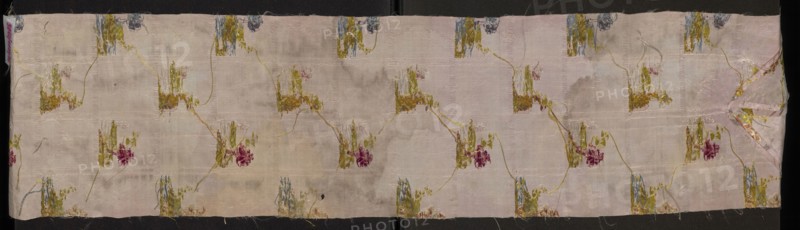 Fragment of pale pink silk fabric brocaded with colorful threads and silver thread. Brocade threads: light green, pink, pale pink, light brown, white, blue, pale purple, cherry red, silver. The fabric is divided into horizontal silver stripes forming the basis for miniature landscapes placed alternately: a tuft from which a tree grows, smaller silhouettes of trees in the background, and a fragment of ruins overgrown with vegetation. These landscapes are separated by vertical stripes and floral bouquets woven from the background. The fabric background is a weave derived from linen a type of rep. 2nd half of the 18th century, France. Height 106 cm, width 23 cm., A long rectangular piece of fabric with a pale pink background shows a repeating floral motif connected by thin curving stems; the motifs include shades of olive green, mustard yellow, muted blue, and deep rose, with hints of beige and cream where the base shows through, and the fabric surface displays areas of wear and faint dis...