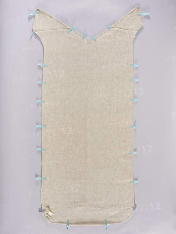 Back of the chasuble, fabrics, metal threads, liturgical vestments, Turkish fabrics, fragments of silk fabrics, patterned fabrics, flowers, leaves, plant ornaments, church paraments, sacred art, churches and chapels furnishings. The back of the chasuble is sewn from two fragments of fabric with motifs of large palmettes placed on a plain red background. The palmettes with serrated edges are decorated inside with floral sprigs and fruit spreading symmetrically and enclosing a smaller palmette with arabesque patterns in the center. Patterns in cream, blue, and gold. Three pieces of fabric sewn into one. Regular plant ornament, unfolding vertically on a red background. Colors: gold, white and sapphire. 17th century, Turkey. Liturgical vestment; length 118 cm, width 49 cm back., A long rectangular fabric piece with a V-shaped notch at the top and rounded corners at the bottom, made of beige woven material, laid flat against a pale gray background, with a few small light blue ribbon loops a...