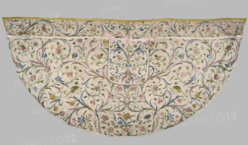 Cope, Cope made of embroidered silk fabric with linen lining; the silk backing of the embroidery has crumbled and the embroidery is preserved thanks to a linen backing hidden beneath the silk. Embroidered decoration entirely covers the surface with a pattern of leafy tendrils and flowers roses, tulips, carnations. Silhouettes of birds — peacocks, parrots, turkeys, and others — adorn the branches. Edges trimmed with yellow silk braid; hood features preserved bows of pink silk ribbon. 18th century, Silesia. Liturgical vestment. Dimensions: length 139 cm, width 287 cm., A semicircular textile with an off-white background densely covered in an allover floral and foliate embroidery, showing a symmetrical swirling vine pattern with a few large stylized flowers and several smaller blossoms in pastel pink, pale blue, soft yellow, muted green, and touches of purple and gold; the vines and leaves are mainly green with accents of blue and purple, and there are a few bird motifs embroidered in gre...