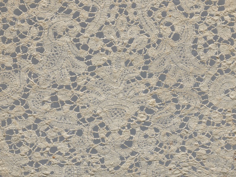 Lace fragment., With floral vase motifs with flower branches in a candelabra arrangement. Joints with picots. Gently serrated lower edge. Lower edge with a ladder. 17th century, Brussels. Lace, fabric; width 21 cm, length 162 cm., A close-up view of a piece of lace fabric showing a repeating openwork pattern with irregular holes and interconnected motifs, made of off-white or cream-colored threads against a muted gray background; the lace has a textured, slightly raised surface with areas of denser stitching and finer net-like sections, and there are a few small darker brownish spots scattered on the fabric.