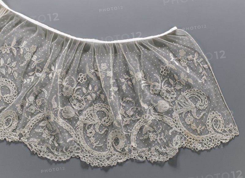 Collar; Lace collar so-called berta with a pattern of flowers, leaves and small dots in the background; floral and plant ornaments; women's clothing accessory; 1840–1860; Brussels place of origin?; lace; width 33 cm., A length of delicate sheer fabric with embroidered floral and scrollwork patterns laid flat against a smooth background; the fabric is translucent with a dotted mesh and ornate lace motifs along the scalloped edge, showing embroidered leaves, flowers, and swirling shapes; the visible colors are shades of off-white and cream for the lace and embroidery, pale beige highlights, a translucent whitish appearance in the mesh, and a muted gray background.