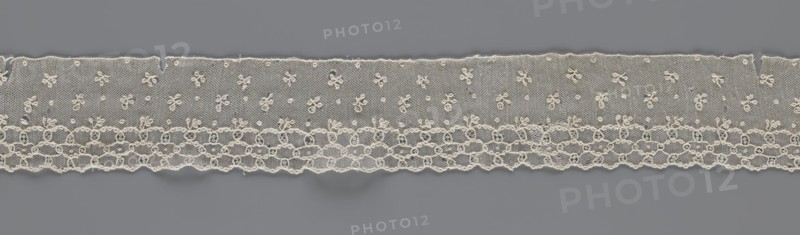 Lace fragment, lace; Edge ornament on one side — a kind of net with numerous loops, small round and slightly larger oval ones, into which small twigs are woven. Above the edge ornament, against the netting background, in regular projections alternate: a twig and a round point. 18th–19th century, France. Materials: lace, fabric. Width 8.5 cm, length 408 cm., A strip of delicate lace in off-white laid horizontally against a smooth gray background, featuring a sheer mesh upper section dotted with a scattered pattern of small floral motifs and tiny raised loops, a lower decorative band of interconnected circular and looped designs forming a scalloped edge, and fine threadwork with subtle irregularities and loose fibers visible along the top and bottom edges.