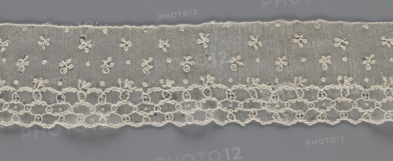 Lace fragment, lace, Edge ornament on one side - a kind of net with numerous loops, small, round and slightly larger oval ones, into which small twigs are woven. Above the edge ornament, against the netting background, in regular projections alternate: a twig and a round point. 18th–19th century, France, lace, fabric, width 8.5 cm, length 408 cm, A horizontal strip of delicate lace in off-white displayed against a smooth medium-gray background, showing a fine hexagonal mesh with a scattering of small floral motifs made from looped stitches and tiny round accents across the upper portion, and a denser lower border featuring interconnected oval and circular motifs with scalloped edge detailing; the lace shows slight irregularities along its top and bottom edges and subtle shadows where it meets the background.