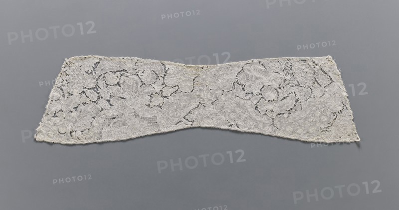 Collar, lace clothing accessory; early 18th century, Binche. Lace, width 15 cm, length 57 cm. Background fond de neige, de brides and others. With large and small floral motifs, ribbons and candelabra., A long, narrow piece of intricately patterned lace displayed flat against a smooth background, showing a floral and scrollwork design with openwork areas and dense embroidered sections; the lace appears off-white or cream with subtle variations in shade, and the background is a uniform mid-gray.