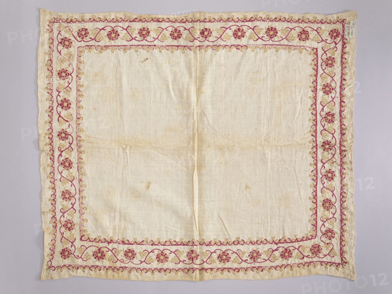 Church napkin. Napkin of white linen canvas edged with a band embroidered with silk and gold thread. Around the edges is a floral and vine motif framed at the top and bottom by a stylized clover ornament. The embroidery is single-sided, pierced; the gold thread on the left side has only a silk core and is unbraided. Dominant colors: magenta and gold. Density: 29 weft threads and 25 warp threads per 1 cm. 17th/18th century, Poland. Fabrics. Height 75 cm, width 63 cm.,  noted. Church paraments; used in Evangelical church furnishings; sacred art., A square piece of light-colored fabric with a decorative embroidered border; the central area is plain and slightly wrinkled with some faint spots and discoloration. The border features a floral vine motif in shades of pink and gold, forming an inner rectangular frame and an outer margin that mirror each other. The flowers are stylized and repeated along the edges, connected by curving stems and small rounded decorative elements. The fabric edge...