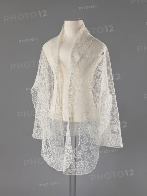 Cape, lace, message provenance, clothing accessories, women's clothing, fashion, capes, 19th century, Europe, clothing accessories, length 75 cm, width 192.5 cm, A display mannequin draped with a delicate lace shawl or scarf, the fabric appearing sheer and intricately patterned with floral and looping motifs; the garment has a soft, off-white to ivory tone with translucent sections showing the lace's openwork, and the mannequin is a pale cream color; the background is a smooth, mid-gray color, and a slim, darker gray stand is visible beneath the mannequin.