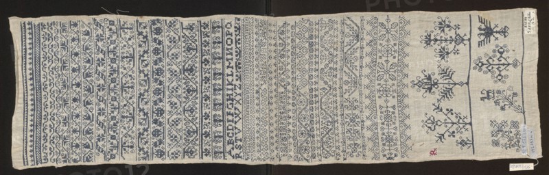 Embroidery sampler, Sampler with a cross-stitch pattern of trails, flower bushes, and letters. Blue embroidery on white canvas. Geometric and floral ornaments with geometrized twigs and leaves; several larger motifs along one edge in the form of stylized flower bushes. Corner features the silhouette of a double-headed eagle. Between the paths, next to geometrical flower tendrils of various types, is a double Holbein stitch ornament. 17th century, Silesia. Embroidery on fabric; height 81.5 cm, width 23 cm., A long rectangular piece of fabric laid flat showing a dense array of horizontal embroidered bands and motifs. The fabric is a light beige or off-white and the embroidery is primarily a dark blue, with a small area of red stitching near one edge. On one side there are several narrow borders with repeating geometric and floral motifs, while the central area contains rows of varied ornamental patterns including stylized flowers, vines, and abstract shapes worked in the dark blue thread...