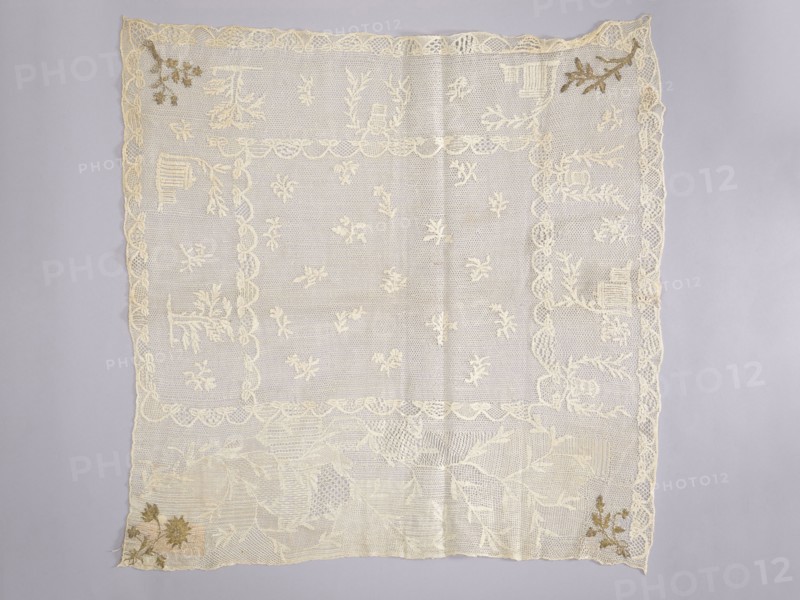 Tablecloth. Embroidered tablecloth; white embroidery on white mesh with gold-thread accents in stitched stitches. Central motifs of small floral sprigs. Three edges feature motifs of trees and houses; the fourth, widest edge has a wide twig motif. Corners show four different floral or leafy sprigs. 18th century, Poland. Materials: fabrics. Dimensions: height 65 cm, width 66 cm., Function: church parament / sacred art church furnishings., A square piece of lace fabric lies flat against a pale gray background, showing an overall cream color with a few tan and brown embroidered accents at two corners. The lace has a scalloped border and an inner rectangular frame, both in cream, with a delicate netted pattern filling the central area. Scattered throughout the central field are several small floral motifs in cream, and larger floral and leafy designs appear near the edges and corners. The lower area features a denser arrangement of lace patterns with overlapping leaves and textured netting...