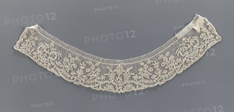 Collar, 19th century, France, band-shaped, equal width, arched with slightly serrated outer edge following the ornament forms. Ornament of floral motifs placed on a mesh background. Materials/technique: lace; function: clothing accessory. Dimensions: width 5.2 cm, length 37 cm., A delicate semicircular lace collar in off-white with intricate floral and scrollwork embroidery laid flat against a muted gray background, showing a mesh ground with denser embroidered motifs along the lower edge and a narrow patterned band along the inner curve; the lace features loops, leaves, and flower shapes in off-white thread with fine netting between motifs, and the background appears uniformly gray.