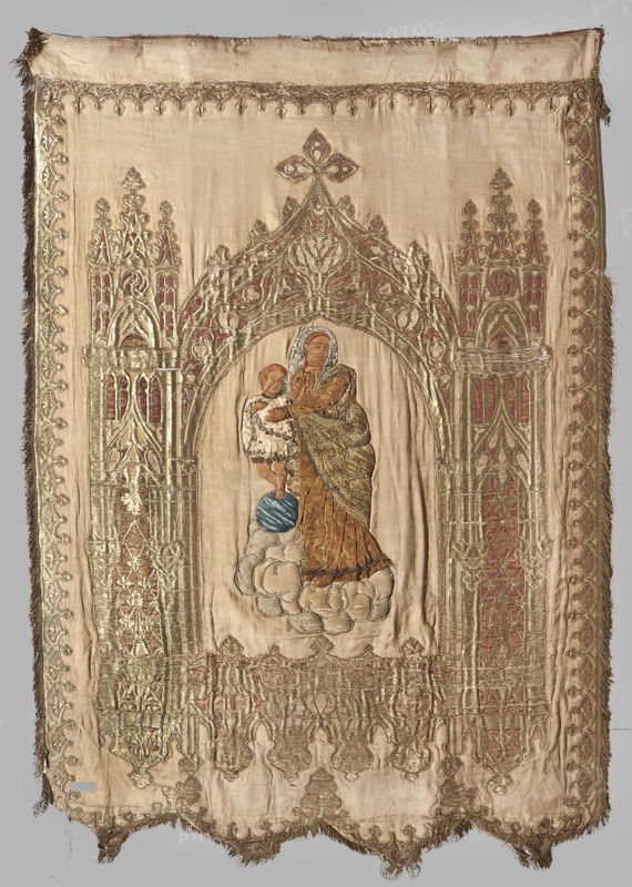 Church banner. Church banner decorated with appliqué and embroidery. Made from fabric elements that form the basis for architectural decoration for figures sewn using the appliqué intarsia method onto a red one side and beige other background. Right side: in the centre of the panel in the neo-Gothic arcade, between two towers, a figure of Mary and Child floating on clouds. Left side: in a similar architectural frame that is an already woven pattern, a figure of the bishop in pontifical robes St. Nicholas . Colors: the panel with the figure of Mary is sand-colored, the panel with the bishop is cherry red. The figure of Mary is appliquéd from smaller fragments of velvet fabrics, fragments of patterned silks, paillettes, and beads. The banner's edge is trimmed with gold fringe. The fabric with the arcade has a satin background, embellished and brocaded with metal thread. 19th century, Poland. Materials: fabrics; height 147 cm, width 102 cm., A rectangular embroidered textile panel with fr...