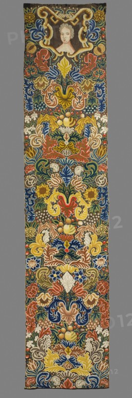 Tapestry embroidered in wool and silk on linen canvas. In the upper part, within a decorative cartouche, is the bust of a lady, her face framed by curls forming a hairstyle. Around it are dense scrolls of large leaves, flowers, and fruit. Unedged. Vivid colors: brown background, green, pink, red, blue, sapphire, and yellow ornament. The plant motifs of the nine fabrics comprising this set do not differ from each other. Stylized leaves, flowers, and fruit fill the entire surface of the panel. The composition unfolds on both sides of the axis, defining a symmetrical division of the decoration, similar to the large-pattern silk upholstery fabrics fashionable in the late 17th and early 18th centuries. Minor differences include the inclusion of small animal silhouettes on some of them, which enrich the decoration. All fabrics are decorated with the same fruit: plump bunches of black and white grapes, yellow apples, and dark red cherries. Vivid colors, brown background, shaded ornament: pink...