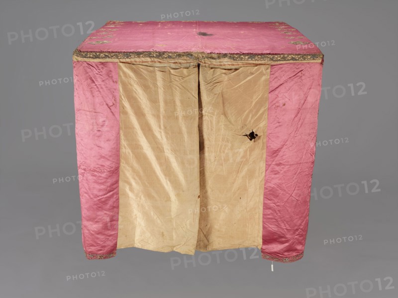 Church cope, liturgical vestment, raspberry satin embroidered with floral patterns. On the front, branch patterns arranged in six rows: two types—asymmetrical, slightly inclined branches with three flowers, and symmetrical, straight branches with a single flower at the top and two pairs of leaves. Edges decorated with a border of floral and fruit tendrils; lower edges trimmed with gold bobbin lace. Beige linen lining. 17th century, Poland. Height 298 cm, width 201 cm., A rectangular cloth structure with a top and front panels is shown, the top and side front panels are pink with a slightly shiny texture and decorative trim along the top edge, and the central front panels are beige with visible creases and a tear in one panel; the fabric appears worn and slightly stained in places, and the background is a uniform gray.