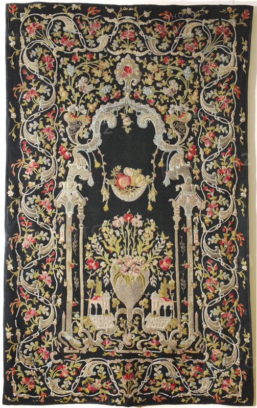 Tapestry, In the center, in an architectural frame modeled after Eastern styles with Rococo elements, is a vase of flowers, flanked by sections of fantasy architecture with an Eastern line. Above is a hanging basket of fruit. The border consists of floral tendrils. Predominant colors are black background with sand, blue, and pink ornament. Appliqués are made of fragments of sparsely woven woolen fabrics; edges of appliqués are embroidered with a needle and silk thread. Some motifs are embroidered with gold thread. Tapestry embroidered and appliquéd with silk and metal threads on a dress, Syria-Damascus, 18th century. Similar 18th-century examples attributed to Syria or Turkey; such tapestries were produced in places like Banja Luka, Bursa, and Istanbul and were intended to decorate tents. Dimensions of a comparable example: height 224 cm, width 142 cm., A large rectangular textile with a dark background covered in an elaborate embroidered design featuring flowing vines, stylized floral...