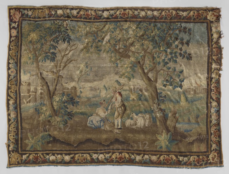 Figural tapestry, flowers, floral ornaments, fruit, trees, pastoral depictions, interior furnishings, tapestries, decorative fabrics, borders, tapestries, weaving. In the center, under the trees, a shepherd with a girl and sheep. In the background, on the left, rural buildings, and on the right, a castle. Border with floral motifs. Colors: green, brown, ochre, and beige. 18th century, France. Fabrics. Height 259 cm, width 340 cm., A worn woven scene framed by a decorative floral border in shades of brown, gold, red, blue, green, and cream shows a pastoral landscape with large leafy trees in green and blue tones, grassy ground in brown and green, and a small body of water with blue highlights. In the foreground a seated figure in muted blue and cream clothing and a standing figure in brown and cream with a red head covering are near a group of white or cream sheep. Background elements include faint structures and fences in muted beige and brown, distant hills in gray and taupe, and scat...