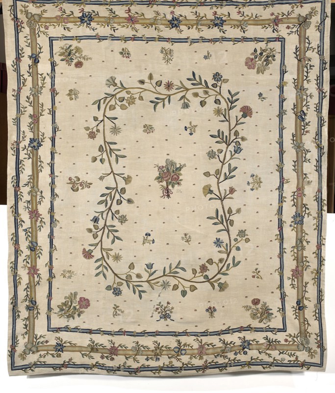 Kilim, Court kilim, decorative fabric kilim with plant and floral patterns. In the center, a small rose bouquet surrounded by a medallion formed by a winding branch with small, various flowers and leaves. The background is decorated with projections of bouquets, flower sprigs, and small geometric ornaments. Large flower bouquets are depicted in the corners. Bordered with three simple frames, each bordered by a winding branch. Colors: white, blue, green, and red. 2nd half of the 18th century. Poland. Height 226 cm; width 192 cm., A large rectangular textile with an off-white background features a decorative border and central floral garland; the border has several layered bands in beige and blue with embroidered vines and a few flowers in blue, pink, yellow, and green, and the interior shows a loose oval of intertwined stems and leaves in green and beige bearing small flowers in blue, pink, yellow, and muted red, with scattered small floral motifs in similar colors across the field and ...