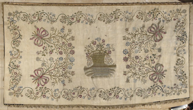 Kilim, Court kilim, 2nd half of the 18th century 18th century, Poland. Woven decorative fabric, height 196 cm, width 392 cm. Court kilim with a central large basket on a decoratively multiplied ground containing flowers on long branches with flying insects. The basket is surrounded by four large flower bouquets placed diagonally. The edge forms a border of a tendril with deep bends created by intertwining flower sprigs. Colors: white, olive green, magenta, and blue. Subjects: floral patterns, basket with flowers, flower bouquets; function: interior furnishing., A rectangular textile with a cream background features an ornate embroidered border of winding vines and flowers in shades of green, muted red, pale blue, gray, and brown; the central area shows a woven basket motif with floral sprays above and flowing ribbon-like botanical branches on either side, the ribbons rendered in pink and muted red tones and the foliage in green, brown, blue, and gray; small scattered floral details and...