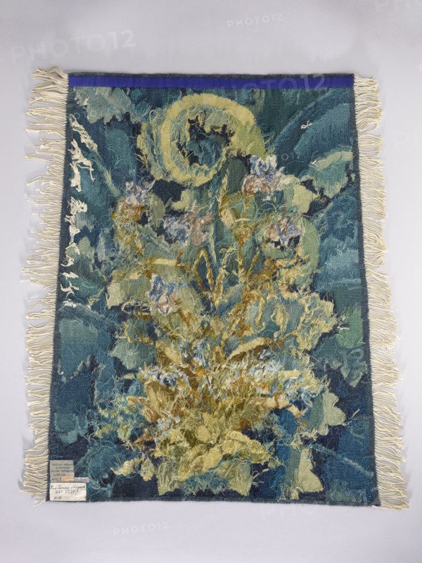 Tapestry coverings;, repossession provenance. Design: leaves, birds, fabrics, borders, interior decorations, interior furnishings, decorative fabrics. Details: a seat — a bird with spread wings among large leaves and flowers; b backrest — flowers among large leaves. Colors: green, blue, yellow, ochre, brown. Date: 1st half of the 20th century. Place of origin: Vienna. Material: fabrics. Dimensions: height 74 cm, width 109 cm., A woven textile with fringed edges laid flat against a pale background, showing a central abstract floral or botanical composition in shades of blue, teal, green, yellow, and cream with textured, loose yarns and tufted areas; the border includes darker blue and teal tones with cream fringe along the sides and bottom, and a narrow strip of deep blue across the top; overall the piece features varied fiber textures, layered threads, and a mix of muted and brighter blues, greens, yellows, and cream colors.
